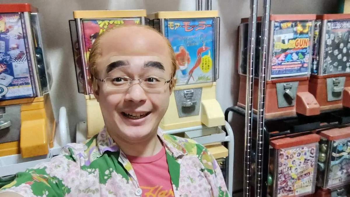 コレクションした往年の販売機の前で笑顔のレッツゴーよしまさ