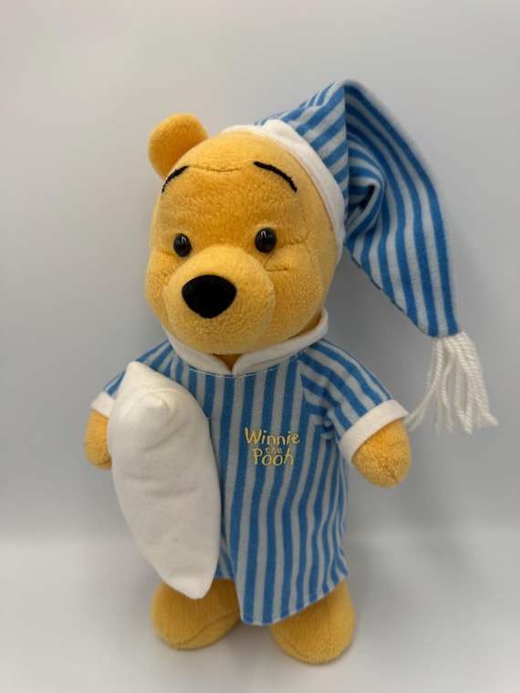 1990 年代のくまのプーさんがパジャマを着てベッドに座り、枕と